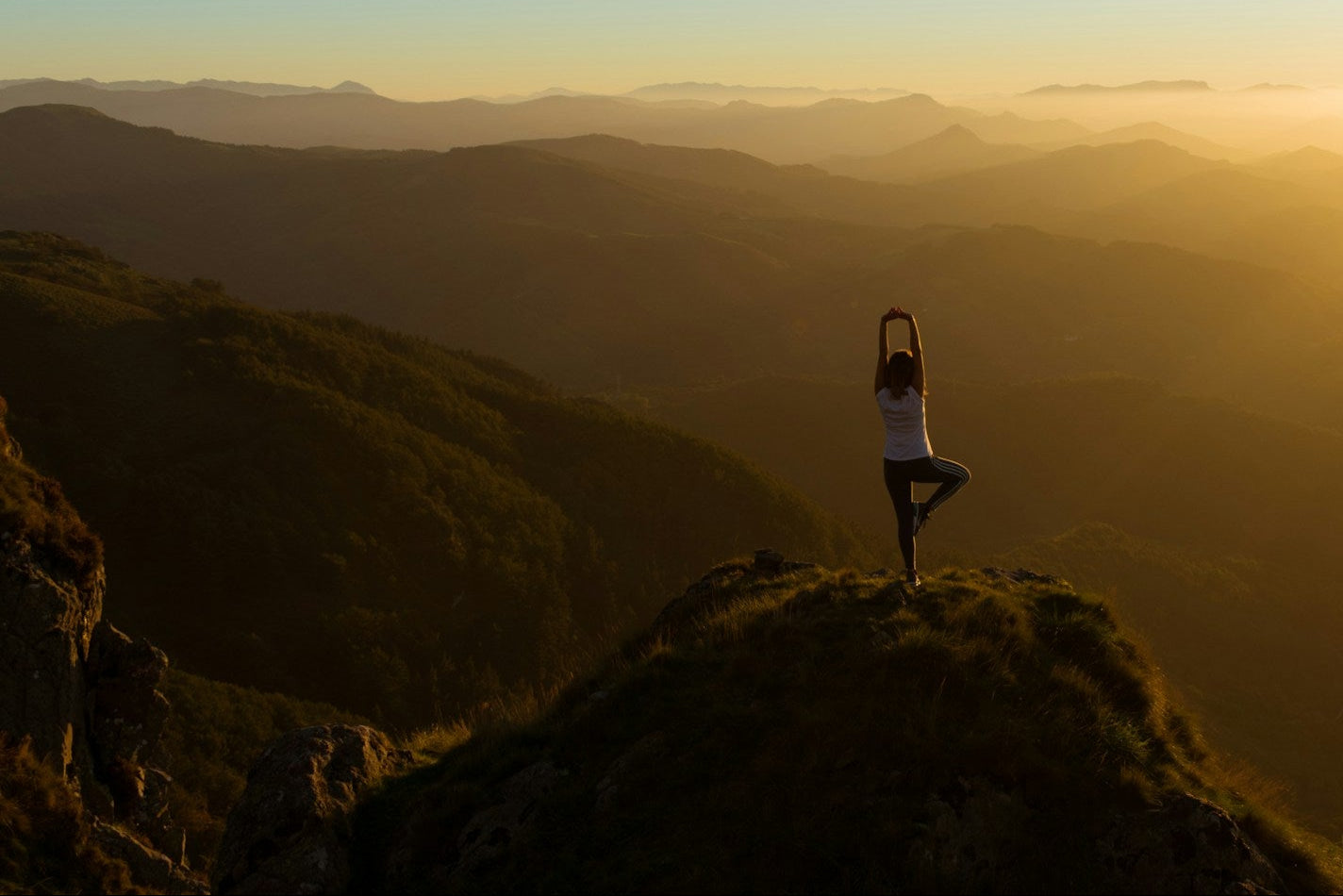 Person practicing yoga on a mountain peak at sunset